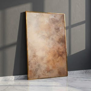 May include: A rectangular wall art piece featuring an abstract painting with blended shades of beige, tan, cream, and brown. The artwork has a visible, textured paint application and is enclosed within a thin, metallic gold-colored frame.