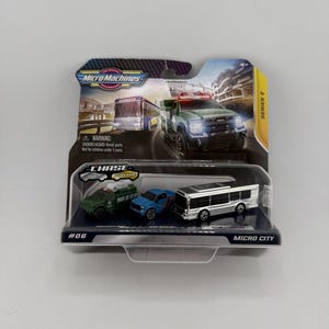 May include: A Micro Machines Series 2 Micro City toy set in original packaging. The set includes three miniature vehicles: a green utility truck, a blue pickup truck, and a silver bus. The packaging features the Micro Machines logo and text.