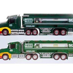 May include: Two toy Hess gasoline tanker trucks. The trucks are dark green with yellow and red accents. The words "HESS" and "GASOLINE" are printed on the side of the tanker. The trucks are sitting on a white surface.