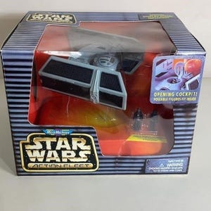 May include: A Star Wars Action Fleet TIE fighter toy in its original box. The box is blue and silver with the Star Wars logo and a clear window showing the toy. The toy is gray and black.