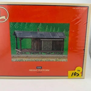 May include: A model freight platform, with a wooden structure and a dark roof, is depicted on a red background. The box includes the text "FREIGHT PLATFORM" and the Lionel logo. The box is labeled "FOR AGES 8 TO ADULT."