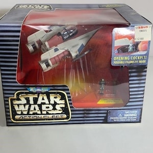 May include: A Star Wars Action Fleet toy set featuring a miniature spacecraft model in a display box. The box has a black and gray striped design with the Star Wars logo and the text "OPENING COCKPIT! POSABLE FIGURES FIT INSIDE".