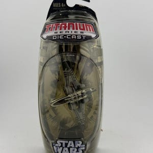 May include: A Star Wars Titanium Series die-cast fighter model in a clear plastic package. The package has a black top with the text "AGES 4+". The model is silver and black.