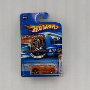 May include: An orange Hot Wheels die-cast car, "Paradigm Shift 2/10", on a blue and white card. The card features the Hot Wheels logo and text "faster than ever". The car is a 2003 First Editions X-Raycers model.