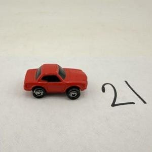 May include: A small red toy car with black windows and black wheels. The car is positioned to the left of the handwritten number 21, which is written in black ink on a plain white surface.