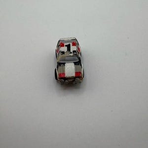 May include: A small toy car with a white, black, and red color scheme. The car has a number 1 on the roof and a white stripe down the center. The toy car is a miniature replica of a race car.