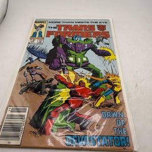 May include: A vintage comic book featuring the Transformers. The cover art depicts a battle scene with robots in various colors, including green, red, and yellow. The title "The Transformers" is prominently displayed, with the text "Dawn of the Devastator!" at the bottom.