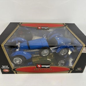 May include: A blue Bugatti model car in a black and gold box. The model is a 1/18 scale replica with detailed silver wheels and a classic design. The box has the brand name "Burago" and "Special Collection" printed on it.