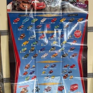May include: A Disney Pixar Cars 2 2011 collector poster featuring a large graphic of Mater and Lightning McQueen at the top. The blue background displays rows of small character car illustrations organized into categories with the text Collect Them All.