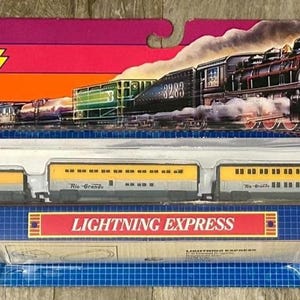 May include: A Micro Machines Lightning Express train set in original packaging. The set includes a locomotive and four passenger cars with yellow and grey bodies, plus ten track pieces. The packaging features a steam train graphic and text.