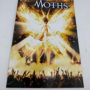 May include: A comic book titled Moths #1 of 6 by J. Michael Straczynski and Mike Choi. The cover features a central figure glowing with bright yellow light in the shape of moth wings above a dark crowd of people with their arms raised in the air.