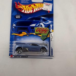 May include: A blue Hot Wheels Backdraft die-cast toy car in its original packaging. The card features the Hot Wheels logo, a graphic of a blue car, and a Race & Win Online promotional sticker. The car has silver wheels and a metallic blue finish.