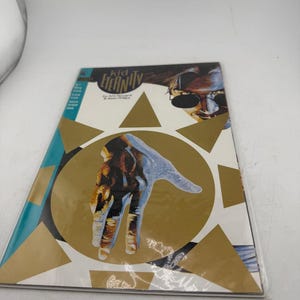 May include: A comic book titled "Kid Eternity" featuring a stylized hand illustration with a gold and blue color scheme. The cover also includes a portrait of a person wearing sunglasses.