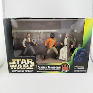 May include: A Star Wars Cantina Showdown action figure set. The box features three figures: Dr. Evazan, Ponda Baba, and Obi-Wan Kenobi. The box has the Star Wars logo and the text "The Power of the Force". The set is for ages 4 and up.