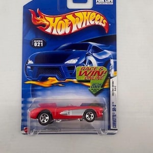 May include: A red Hot Wheels Corvette SR-2 die-cast metal toy car on a blue and white card. The card features the Hot Wheels logo, a flame graphic, and the text "Race & Win!" The car is a convertible.
