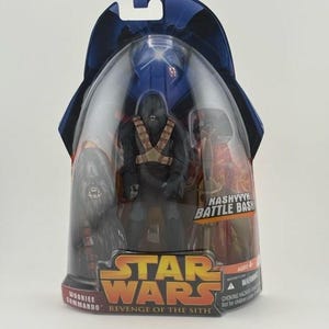 May include: A Star Wars action figure set featuring a Wookiee Commando from Revenge of the Sith. The figure is in a clear plastic package with the Star Wars logo and the words "Kashyyyk Battle Bash". The packaging is blue and black.