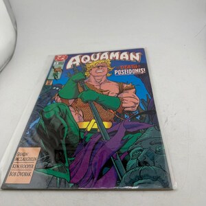May include: A comic book titled Aquaman: The Death of Poseidonis! featuring a blonde character in a green and orange suit holding a trident. The cover art displays the character in a dynamic pose against a blue background with text credits.