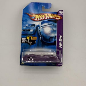 May include: A purple Hot Wheels die-cast car in its original packaging. The packaging is blue and purple with images of cars and the text "Hot Wheels" and "POP-OFFS". The car is a sleek, futuristic design.