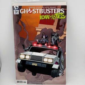 May include: A Ghostbusters comic book in a plastic sleeve. The cover features a stylized illustration of the Ghostbusters' vehicle with characters and the title "Ghostbusters" and "IDW 20/20". The background is a mix of orange and brown.
