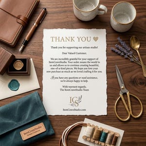 May include: A thank you note from ItemCraveStudio on textured paper with deckled edges, surrounded by a brown leather notebook, a fountain pen, two speckled mugs, a gold spoon, scissors, a teal velvet pouch, and spools of thread on a wooden surface.