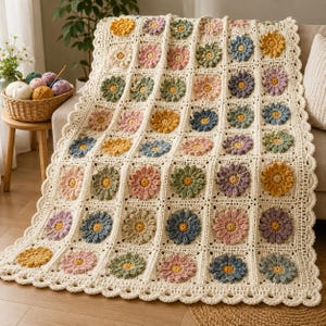 Può includere: Una coperta lavorata all'uncinetto a mano con una griglia di motivi quadrati, ognuno contenente un fiore in rilievo nelle tonalità del giallo, rosa, blu, verde e viola. La coperta ha un colore di base bianco sporco e un bordo smerlato.