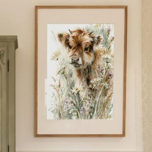 Watercolor highland cow calf printable wall art framed in warm wood displayed in a soft cottagecore nursery with sage green armoire, rattan children's table, rocking toy, and lace curtains — instant digital download farmhouse baby room decor