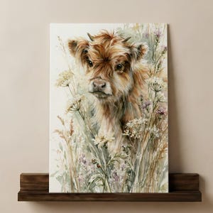 Watercolor highland cow calf print with wildflowers leaning on a dark walnut floating shelf against a warm neutral wall, farmhouse nursery wall art digital printable download instant print at home