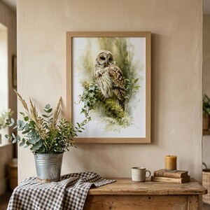 Watercolor owl printable wall art in natural wood frame above rustic farmhouse console table styled with eucalyptus botanicals, gingham cloth, and stacked books in a warm cottagecore entryway setting