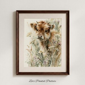 May include: A framed watercolour print featuring a fluffy brown Highland calf surrounded by delicate white and purple wildflowers. The artwork is encased in a dark brown wooden frame with a light beige mat, and the text Zoi's Painted Pasture is below.