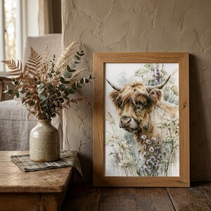 Watercolor highland cow wildflower printable wall art in natural oak frame leaning against textured plaster wall styled with dried botanicals and ceramic vase in rustic farmhouse cottagecore home decor setting