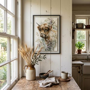 Watercolor highland cow wildflower printable wall art displayed in black frame on white shiplap wall in rustic farmhouse kitchen with dried wheat stems ceramic jug and linen napkin farmhouse cottagecore digital download print