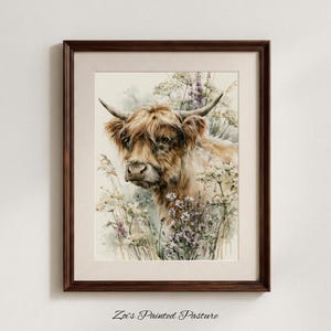 Framed watercolor highland cow print surrounded by wildflowers and lavender, displayed in dark walnut frame with cream mat on neutral gray wall, digital printable farmhouse wall art by Zoi's Painted Pasture