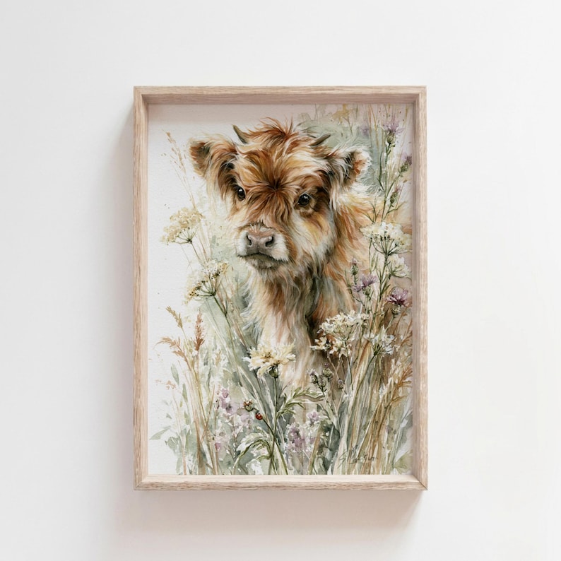 Watercolor highland cow calf printable wall art in natural wood frame on white wall, featuring baby highland cow surrounded by wildflowers and a hidden ladybug, farmhouse nursery decor digital download