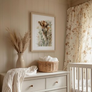 Watercolor highland cow calf printable wall art in natural wood frame displayed above white nursery dresser, cottagecore farmhouse baby room with floral curtains, pampas grass, and wicker basket, instant digital download