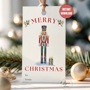 May include: A rectangular white gift tag featuring a red Merry Christmas inscription, a watercolor nutcracker illustration, and a small blue gift box. The tag includes To and From lines, a hole at the top with a tan string, and a red Instant Download badge.