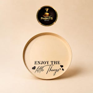 Könnte beinhalten: Ein rundes, hellbeiges Tablett mit dem schwarzen Schriftzug "ENJOY THE little THINGS" und drei kleinen schwarzen Herzsymbolen. Über dem Tablett befindet sich ein kreisförmiges Logo mit goldenem Rand, das den Text "ProjectTS 3D Print" und ein 3D-Drucker-Symbol enthält.