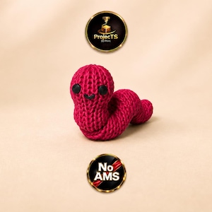 Könnte beinhalten: Eine magentafarbene, 3D-gedruckte Wurmfigur mit einer strukturierten, strickähnlichen Oberfläche. Sie hat zwei kleine, runde schwarze Augen und einen einfachen schwarzen Mund. Über und unter dem Wurm befinden sich kreisförmige Logos mit der Aufschrift ProjectTS 3D Print und No AMS.