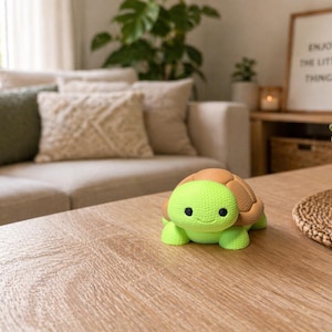 Könnte beinhalten: Eine grüne und braune Schildkrötenfigur sitzt auf einem Holztisch. Die Schildkröte hat einen strukturierten Panzer und ein lächelndes Gesicht. Im Hintergrund ein beiges Sofa mit Kissen und ein gerahmter Druck.