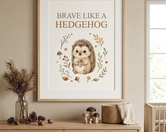 May include: A framed wall art print featuring a cartoon hedgehog holding a mushroom, surrounded by botanical elements and stars. The text BRAVE LIKE A HEDGEHOG is printed in brown and gray above the illustration on a white background.