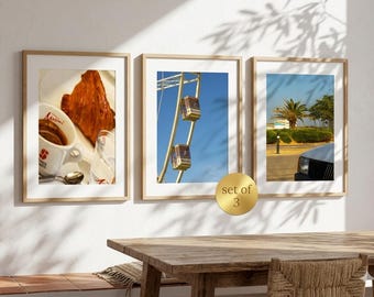 May include: A set of three framed wall art prints. The first print shows a croissant and a cup of coffee. The second print features a ferris wheel against a blue sky. The third print displays a palm tree and a car. A gold circular label reads set of 3.