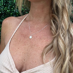 May include: A silver chain necklace with a small seashell pendant. The necklace is worn by a person with long blonde hair.