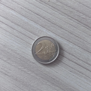 Peut inclure: Une pièce de deux euros au design bimétallique avec un centre doré et un anneau extérieur argenté. La pièce affiche le grand chiffre 2 et le texte EURO, ainsi qu'une carte de l'Europe et des lignes verticales sur le côté droit.