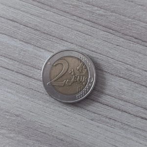 Könnte beinhalten: Eine Zwei-Euro-Münze mit einem silberfarbenen Außenring und einem goldfarbenen Zentrum. Die Münze zeigt die Zahl 2, das Wort EURO und eine Europakarte auf der Vorderseite. Das Design enthält kleine Sterne am Rand des silbernen Rings.