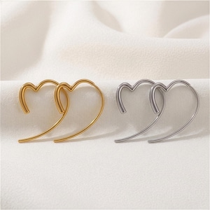 Può includere: Un paio di orecchini a cerchio a forma di cuore color oro e un paio di orecchini a cerchio a forma di cuore color argento. Ogni orecchino presenta una struttura in filo liscio e curvo che forma una silhouette a cuore aperta.