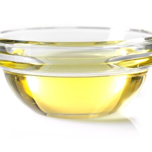 May include: A clear glass bowl filled with a golden yellow liquid, likely oil or vinegar, on a white background.