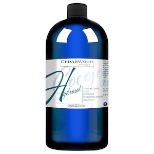 May include: A blue glass bottle with a white label that reads "Cedarwood Hydrosol" and "100% Natural Pure Distilled Cedarwood Water Hydrosol". The label also includes the website cocojojo.com and a Facebook logo.