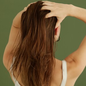 Puede incluir: Una persona con el pelo largo y casta&ntilde;o se muestra de espaldas, con la mano levantada para tocarse el pelo. Lleva un top blanco sin mangas.