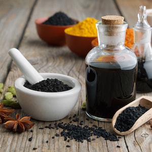 K&ouml;nnte beinhalten: Ein Holztisch mit verschiedenen Gew&uuml;rzen und Kr&auml;utern, darunter schwarze Kreuzk&uuml;mmelsamen, Sternanis, Kardamomkapseln und Zimtstangen. Es gibt auch zwei Glasflaschen gef&uuml;llt mit schwarzem Kreuzk&uuml;mmel&ouml;l und einen wei&szlig;en Keramikm&ouml;rser und St&ouml;&szlig;el mit schwarzen Kreuzk&uuml;mmelsamen darin.