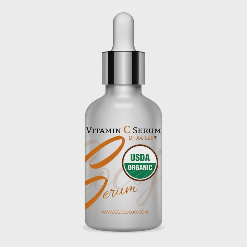 May include: A white Vitamin C serum bottle with a silver cap and dropper. The label includes the text "Vitamin C Serum Dr. Joe Lab" and "USDA Organic". The bottle has orange script and the website address www.cocojojo.com.