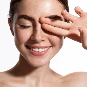 May include: A close-up of a woman's face with freckles, smiling with her eyes closed. Her hand is covering one eye.